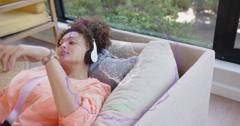 Young woman relaxing with headphones and smartwatch on sofa with digital mesh overlay