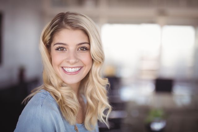 This image features a smiling business woman with blonde hair standing in a creative office environment. She is dressed in casual attire, exuding confidence and professionalism. This photo is ideal for use in business-related content, corporate websites, promotional materials, and articles about workplace culture, female entrepreneurship, and professional success.