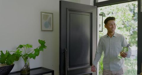 asian man entering home holding water bottle smiling - Download Free Stock Images Pikwizard.com