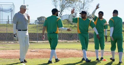 Senior Coach Leading Diverse Baseball Team High-Fiving Players on Sunny Infield Before Game