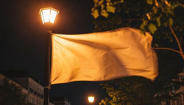 Warm-lit flag billowing from lamppost at night on treelined urban street with amber glow