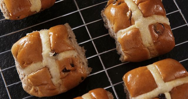This visual showcases freshly baked hot cross buns with a golden-brown crust cooling on a wire rack. Perfect for use in food blogs, recipe books, baking tutorials, and culinary magazines. It captures the essence of traditional Easter and Lenten treats, evoking feelings of warmth, home cooking, and seasonal celebrations. Great for social media posts celebrating holidays or promoting bakery goods.
