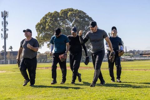 Adult teammates walking across sunny baseball field carrying gloves celebrating camaraderie
