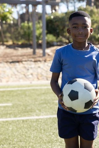 Young african american boy holding soccer ball on sunny turf field