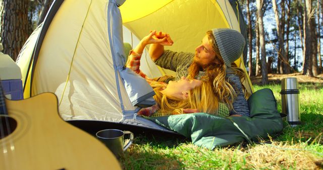 A couple enjoying their time in a camping tent nestled in a forest with a guitar and picnic items outside. Ideal for themes of outdoor adventures, camping holidays, romantic getaways, nature life, and leisure activities. Could be used in travel, lifestyle blogs, adventure promotions, or romantic travel packages.