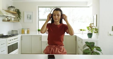 Woman Adjusting Headphones at Kitchen Island Relaxing with Music