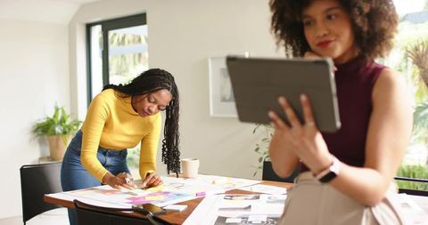 Diverse female team collaborating over sticky notes and tablet in bright creative workspace
