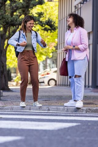 African american women laughing and crossing crosswalk, casual urban friendship moment