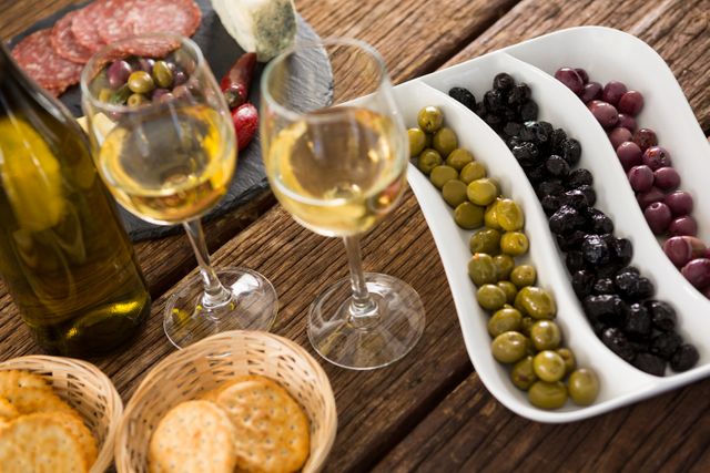 Close-up of a gourmet spread featuring marinated olives, a bottle of wine, and various appetizers on a rustic wooden table. Ideal for use in culinary blogs, restaurant promotions, Mediterranean cuisine advertisements, and food and wine pairing guides.