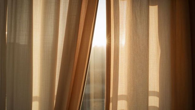 Sunlight streaming through beige sheer curtains with visible dust motes