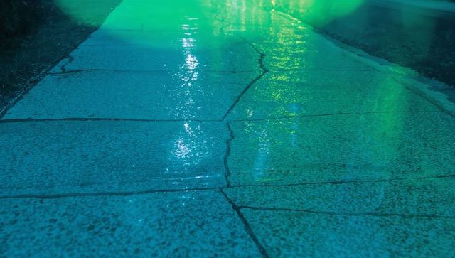 Wet cracked sidewalk with colored reflective light at night