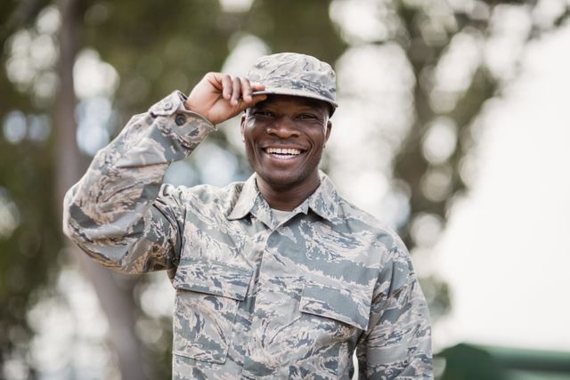 Smiling military soldier in camouflage uniform outdoors, showing pride and dedication. Ideal for use in articles about military life, recruitment campaigns, patriotic events, and training programs.