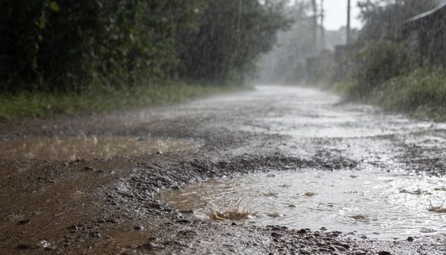 Rain-drenched dirt road with splashing puddle and muddy potholes