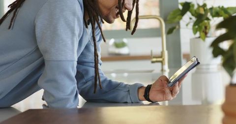 African american man leaning on kitchen island holding tablet, reading and smiling