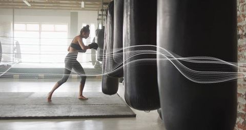Backlit female boxer punching heavy bag in industrial gym strength training cardio