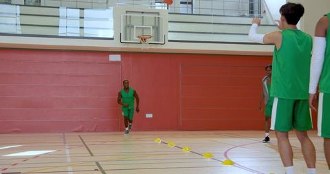 Diverse teammates practicing dribbling and shooting through cones on indoor court