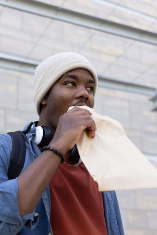 African american commuter eating on the go wearing beanie and headphones holding paper bag