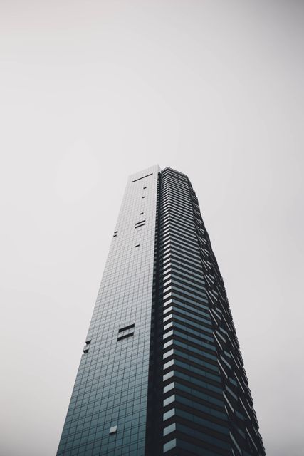 Low angle view showing modern skyscraper with sleek design against clear sky. Ideal for use in real estate promotions, business presentations, and articles on urban development. Suitable for websites related to architecture, corporate offices, and city landscapes.