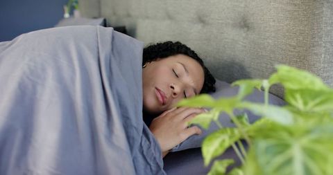 African american woman sleeping peacefully under gray duvet in serene plant-filled bedroom