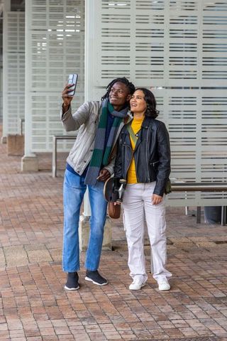 Young couple taking selfie at transit plaza with smartphone and skateboard, urban lifestyle