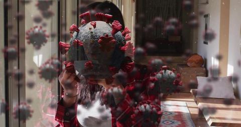 Woman holding coronavirus model covering face through glass reflection, quarantine concept