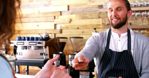Smiling barista accepting credit card payment in trendy cafe
