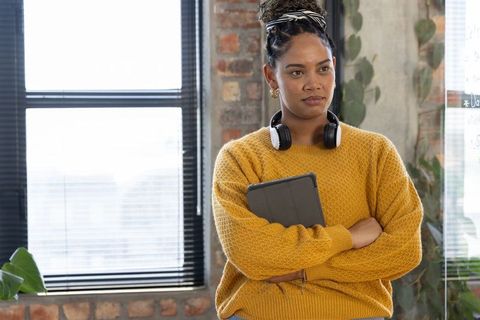Confident african american woman in office holding tablet and headphones