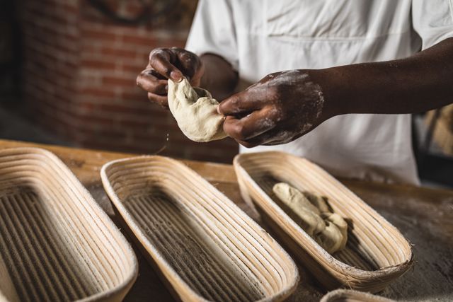 African American baker preparing dough at a kitchen counter in an artisan bakery. Ideal for use in articles or advertisements related to baking, culinary arts, traditional bread making, and the food and drink industry. Highlights skilled craftsmanship and the hands-on process of creating handmade bread.