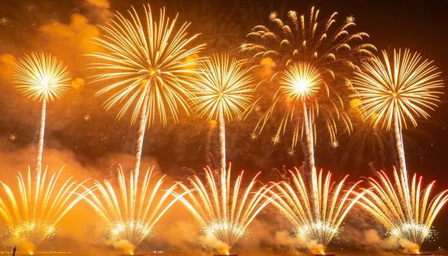 Golden fireworks spectacle lighting night sky over harbor with fountains and comet trails