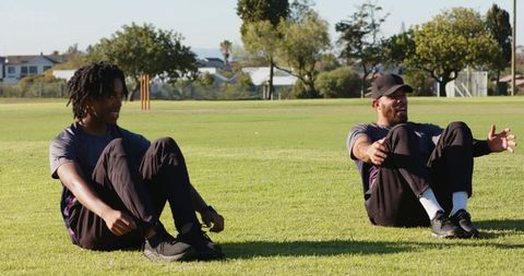 Multiracial men doing outdoor core workout on grass field with trainer guiding exercises