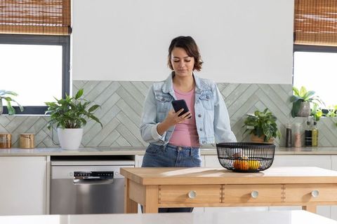 African american woman standing at kitchen island checking smartphone in denim jacket