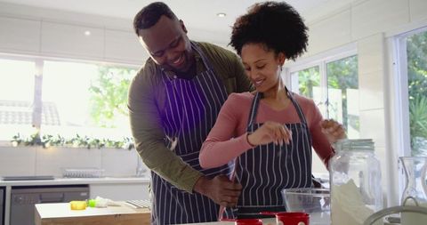Black Couple Baking Together in Cozy Modern Kitchen, Tying Apron and Reaching for Flour