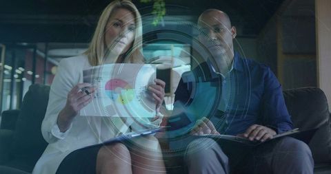 Business partners reviewing interactive dashboard overlay, collaborating on financial report