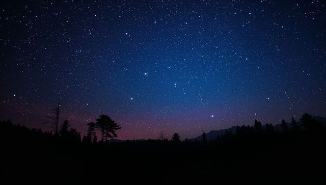 Sparkling starfield over pine forest silhouette and distant mountain ridge at twilight