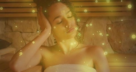 Serene woman relaxing in wood sauna with towel, warm amber glow and bokeh lights