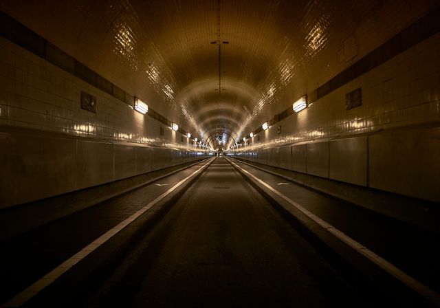 Visual depiction of an empty tunnel with evenly spaced lighting creating a symmetrical perspective. Ideal for projects related to urban infrastructure, architectural design, city planning, transportation, and light studies.