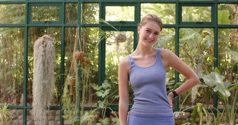 Smiling Woman in Sportswear Standing in Glasshouse Garden