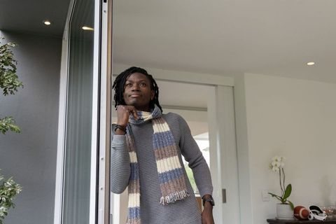 Contemplative african american man leaning in sliding doorway wearing striped winter scarf