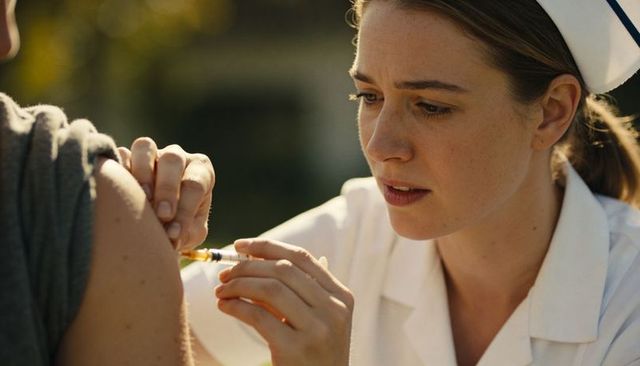 Clinic nurse administering vaccine into upper arm outdoors daytime community vaccination