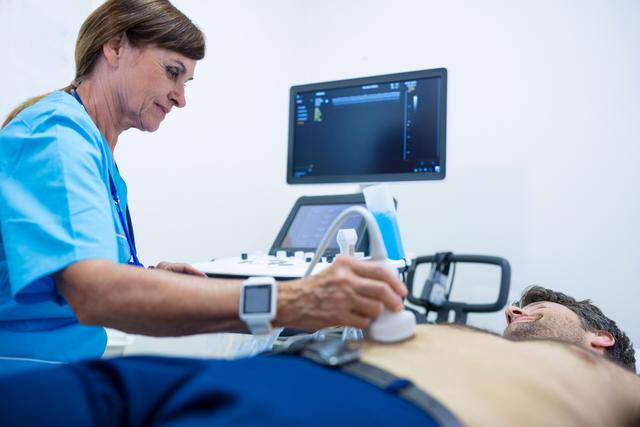 Doctor in blue scrubs using ultrasound machine to examine male patient's abdomen. Useful for healthcare industry, medical technology, patient care, hospital services, and diagnostic imaging topics.