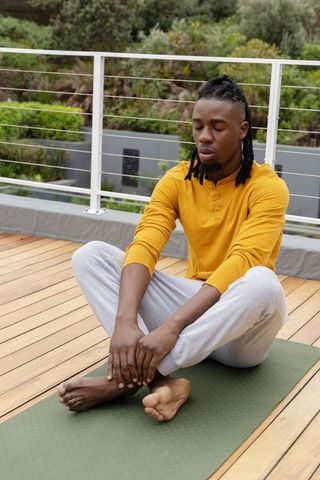 African american man meditating on rooftop terrace wearing yellow shirt and gray pants
