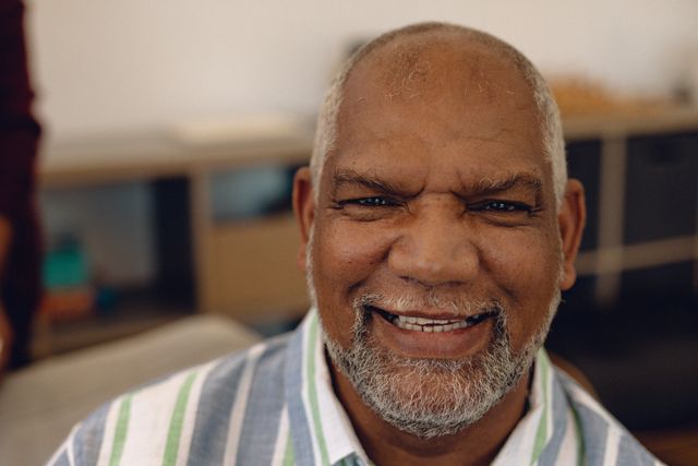 Close-up portrait of smiling biracial senior man with beard in nursing home. Unaltered, support, assisted living and retirement concept.