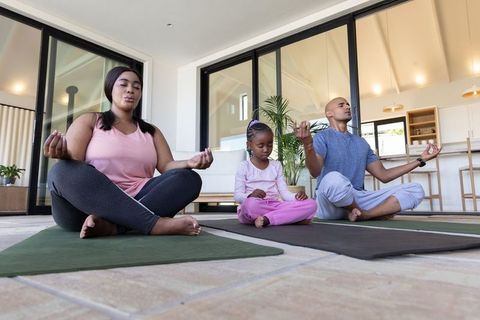 Diverse family meditating together on yoga mats in sunlit open-plan family room