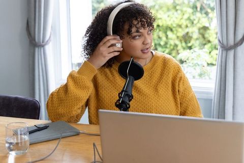 Woman adjusting headphones while recording podcast with laptop microphone in natural light