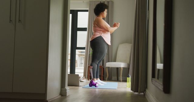 Woman practicing yoga at home stands on yoga mat in quiet room. Ideal for use in wellness blogs, fitness websites, and promotional material for home exercise equipment and healthy lifestyle content.