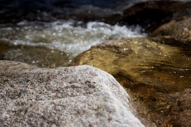This tranquil image captures a close-up view of a stream flowing over rocks, with clear water rushing through the natural setting. It is suitable for use in nature articles, outdoor adventure blogs, environmental projects, or as a harmonious background for presentations.