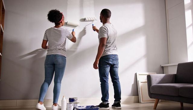 Couple painting living room wall together rolling paint during diy home renovation