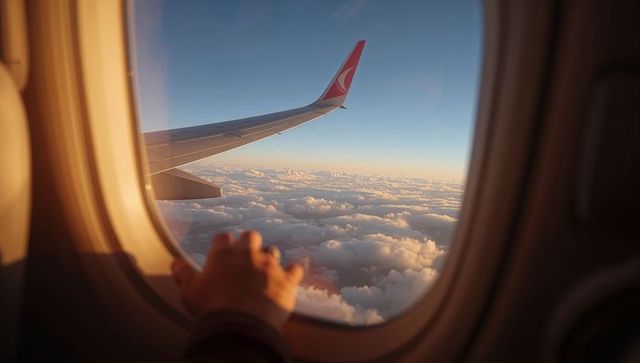 Warm sunlit airplane window view with hand on sill, winglet above clouds at golden hour