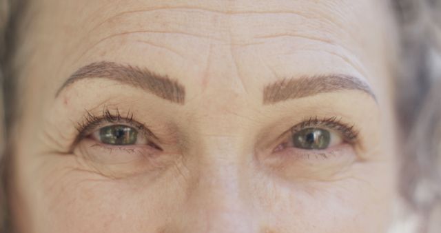 Close-up image of a mature woman's eyes, showing natural wrinkles and defined eyebrows. This can be used in beauty and skincare promotions, healthy aging campaigns, or emphasizing positive and realistic representations of older adults. Ideal for articles or advertisements focusing on eye care, wrinkle treatments, and natural beauty.