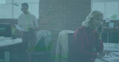 Businesswoman speaking on handset and typing at open-plan desk in modern brick office